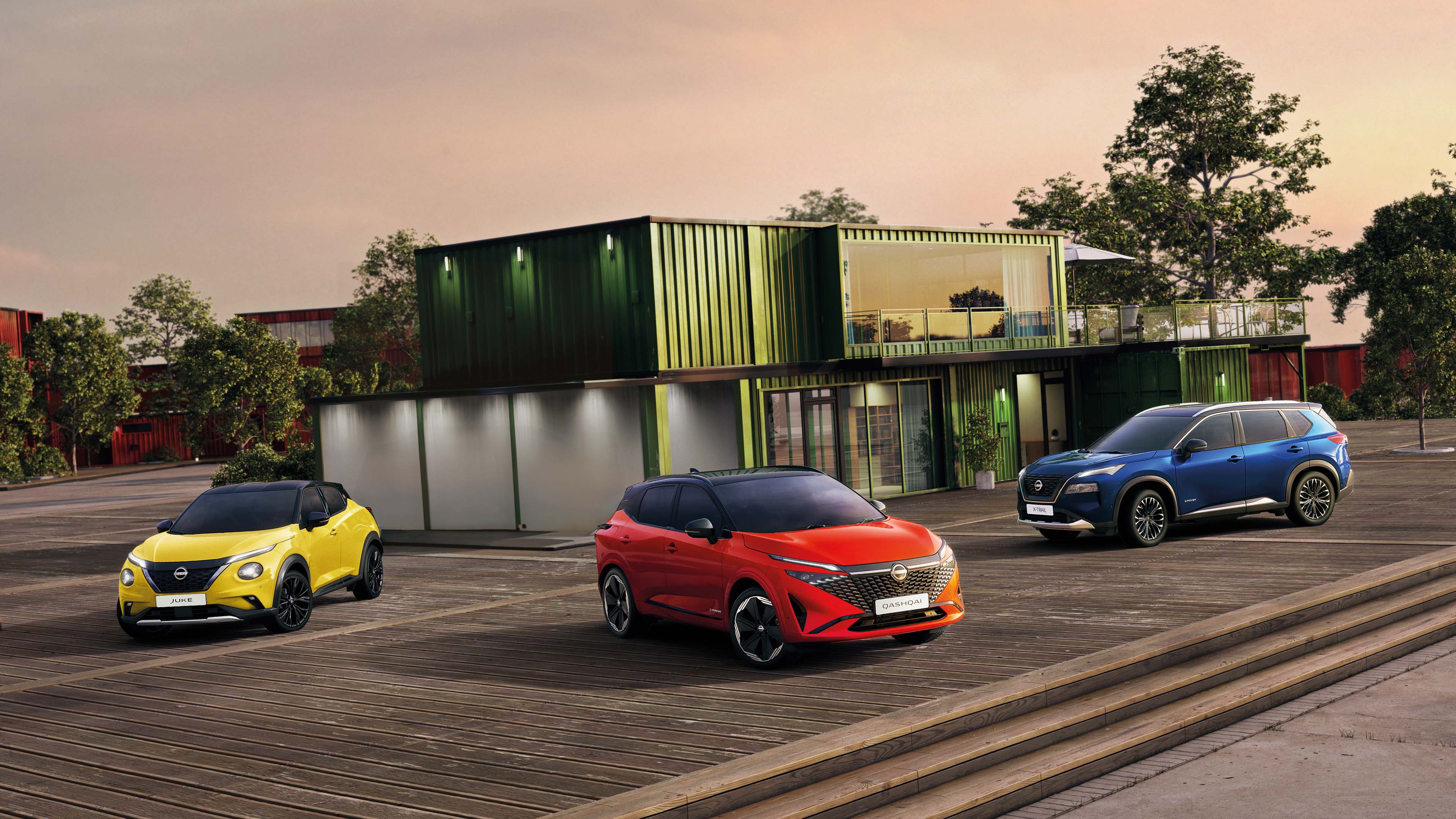 Tri Nissan automobila – Juke, Qashqai i X-Trail – parkirana ispred modernih zelenih modularnih zgrada u zalasku sunca.