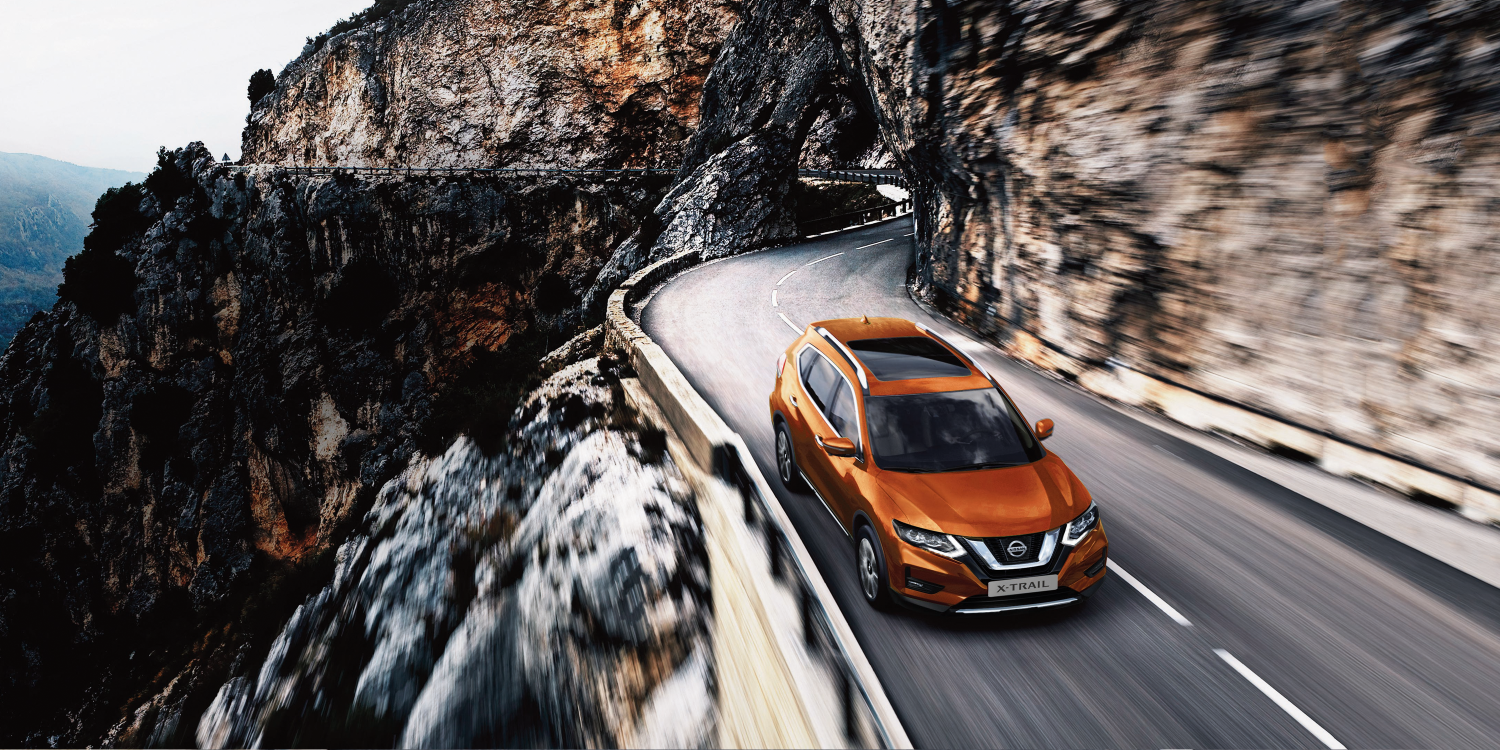 Vue de 3/4 de face et de dessus d’un Nissan X-TRAIL sur une route de montagne - début
