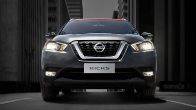 Նարնջագույն և մոխրագույն Nissan Kicks-ի արտաքին տեսքն առջևից քաղաքային փողոցի վրա