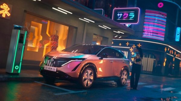 3/4-Nachtaufnahme des Nissan ARIYA beim Laden mit einer Frau