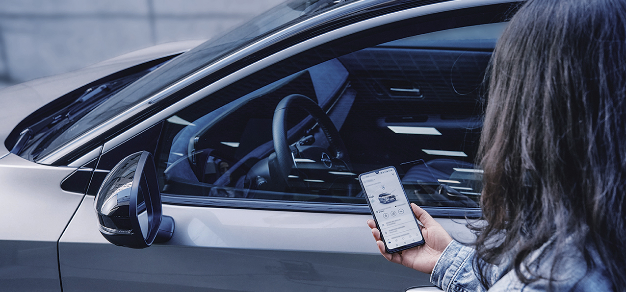 Osoba koristi mobilnu aplikaciju za upravljanje vozilom pored parkiranog automobila
