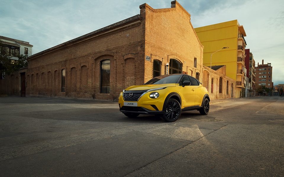 Gelber Nissan Juke parkt vor einem großen Steinbogen in einer ländlichen Umgebung bei Sonnenuntergang.