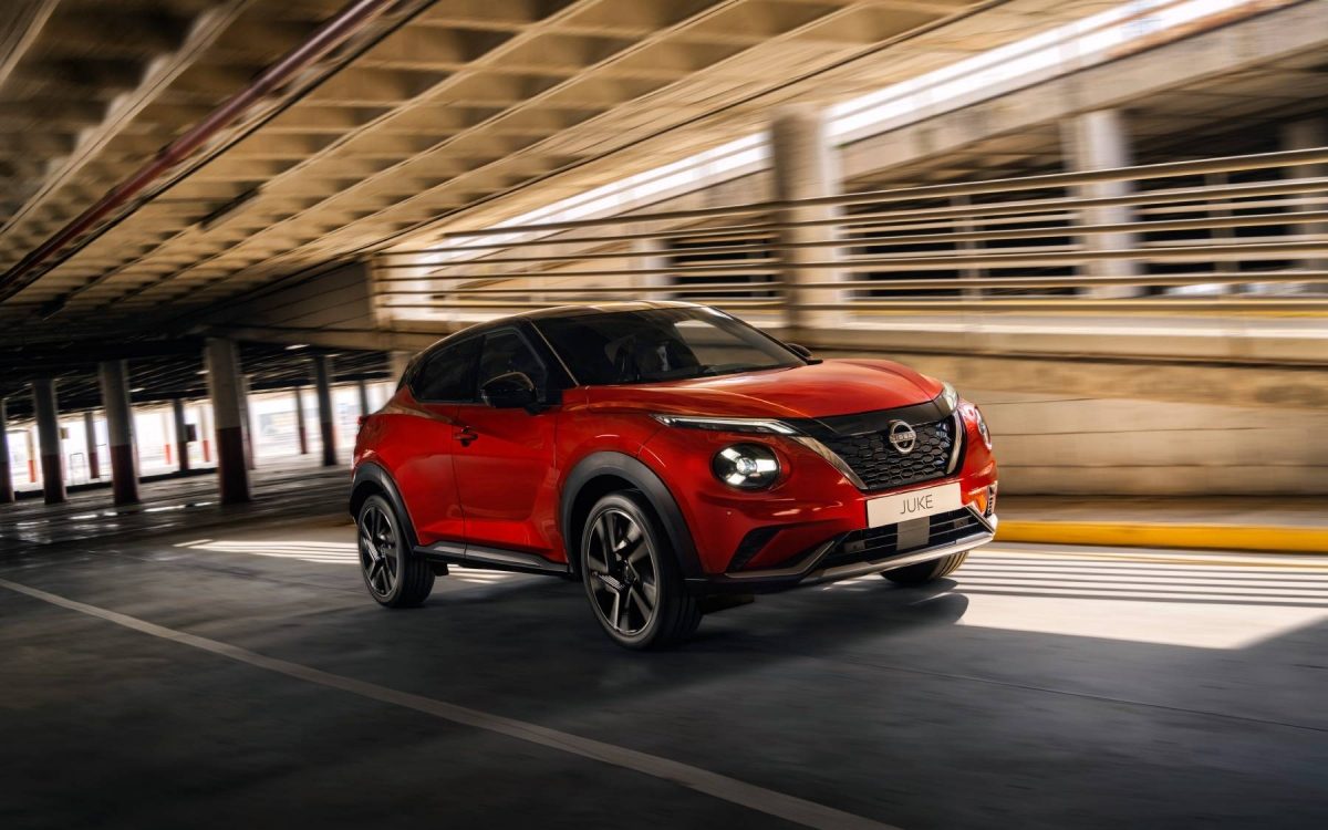 Gelber Nissan Juke parkt vor einem großen Steinbogen in einer ländlichen Umgebung bei Sonnenuntergang.