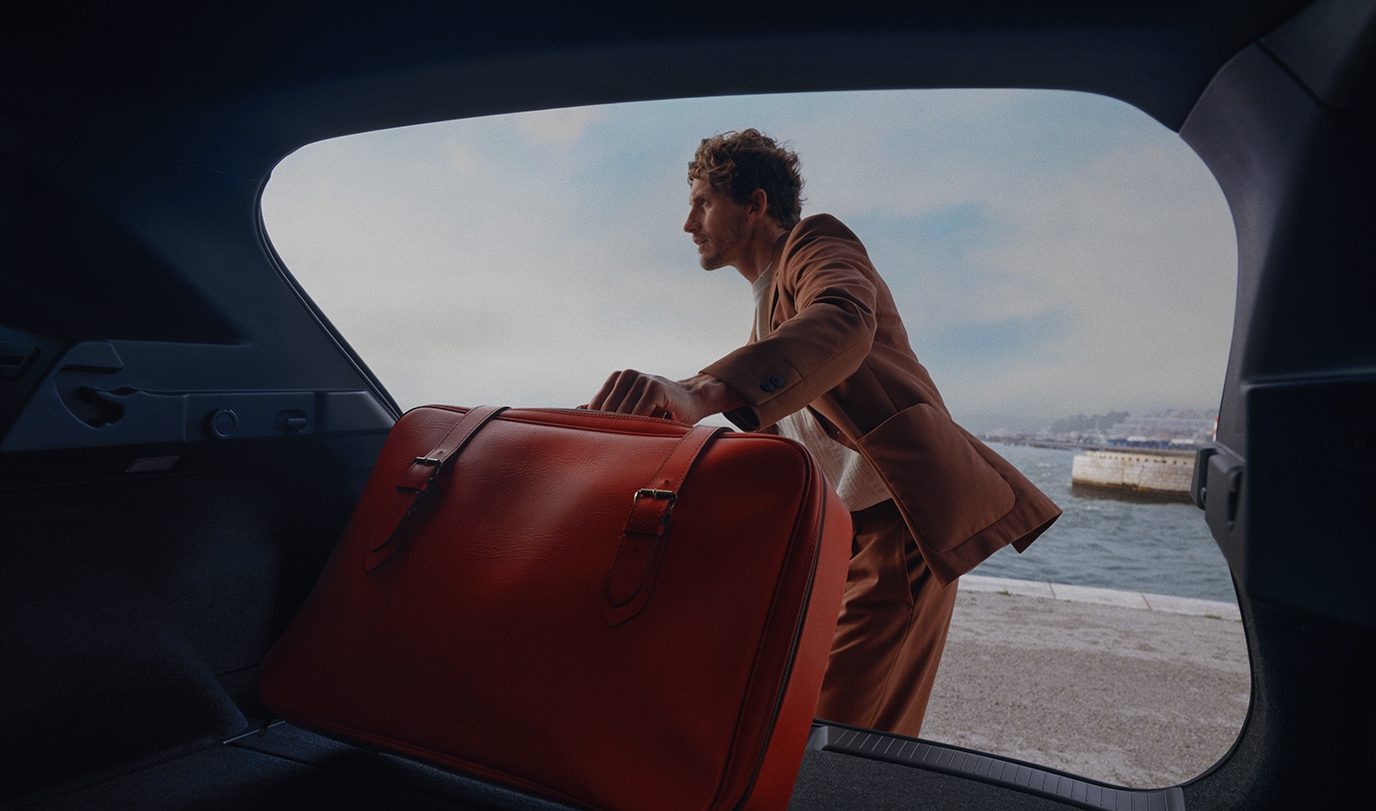 Mann in braunem Anzug holt eine große braune Tasche aus dem Kofferraum eines Nissan Juke.
