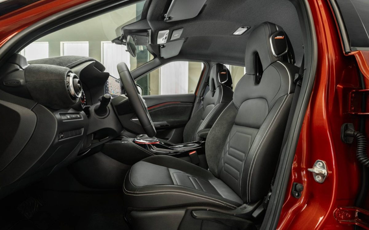 Ein Mädchen blickt zwischen den Vordersitzen eines Nissan Juke mit schwarzem Leder und gelben Akzenten in die Kamera.