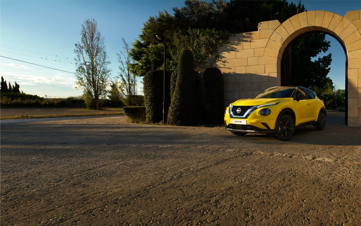 Gelber Nissan Juke parkt vor einem großen Steinbogen in einer ländlichen Umgebung bei Sonnenuntergang.