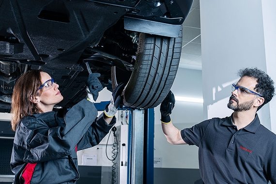 Zwei Mechaniker prüfen ein angehobenes Auto am Rad.