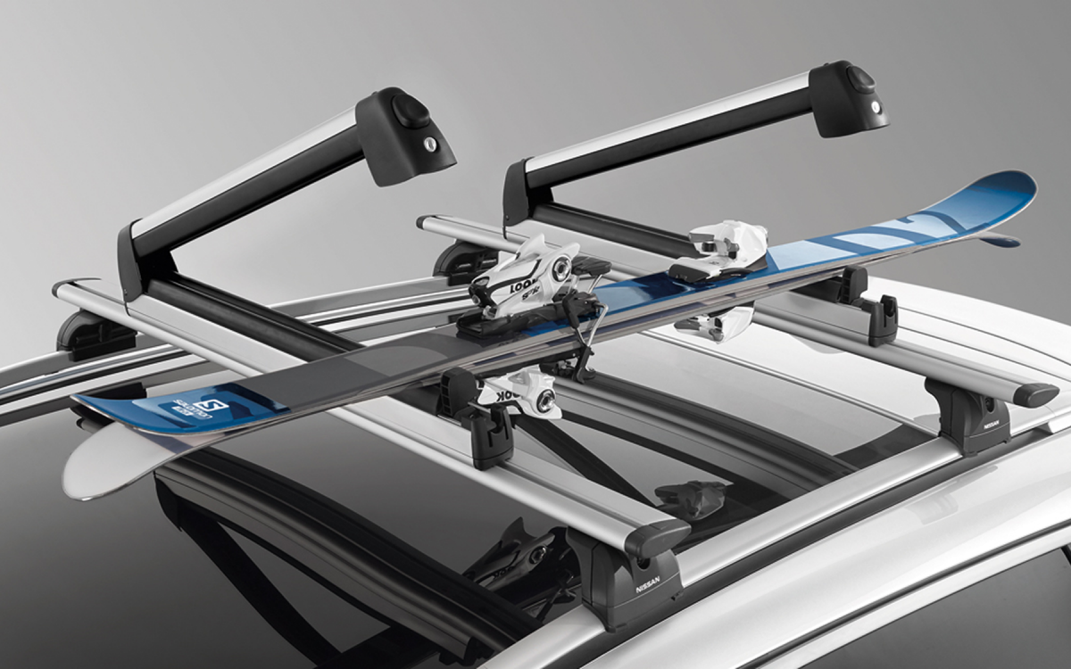 Geöffnete Skiträger mit eingelegten Skiern auf dem Dach eines Nissan montiert.