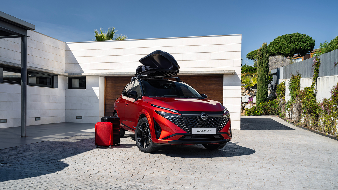 Roter Nissan Qashqai mit montierter Dachbox in einem gepflasterten Hof vor einer weißen Garage.