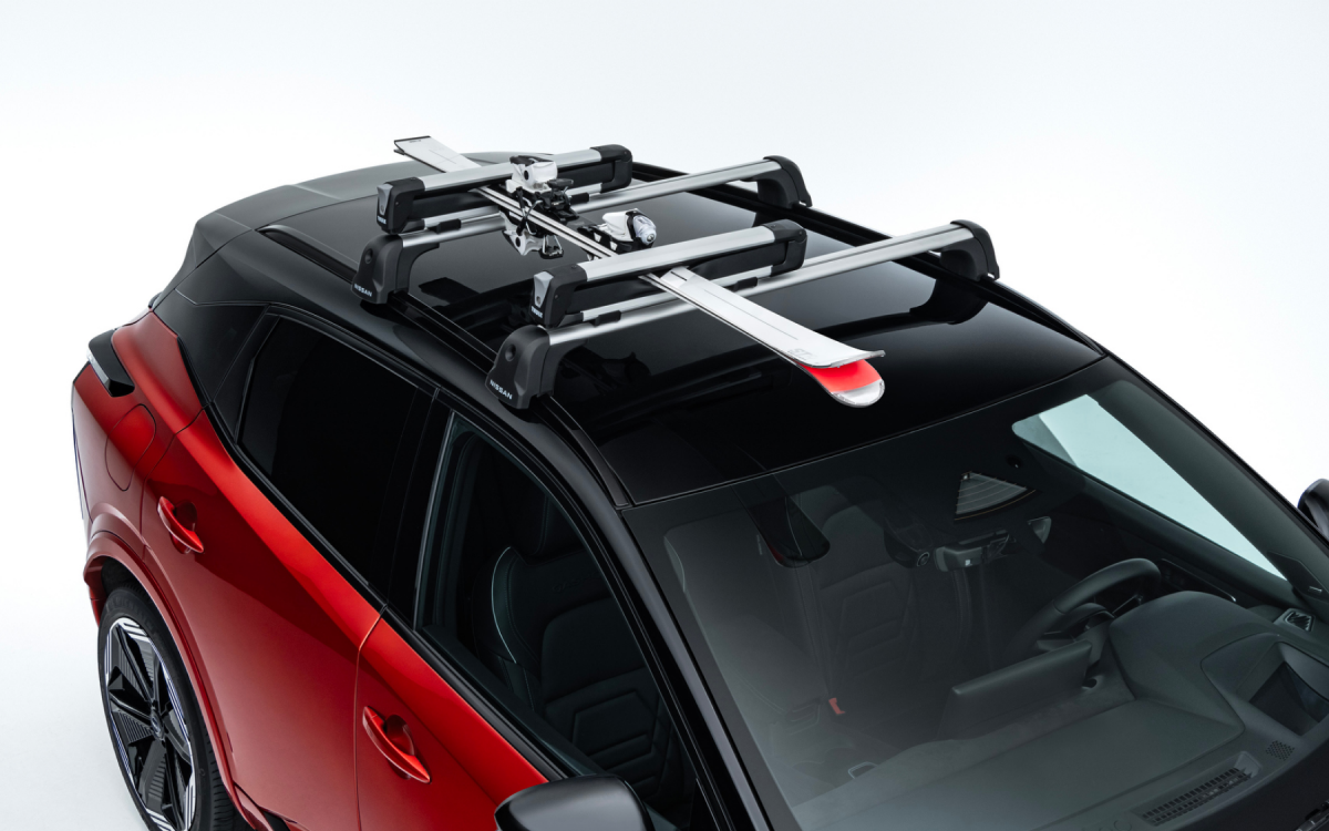 Skiträger mit eingelegten Skiern auf dem Dach eines roten Nissan Qashqai montiert.
