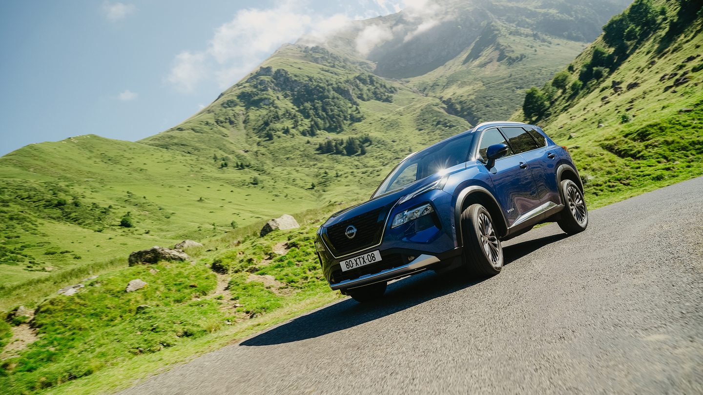 Blauer Nissan X-Trail vor einer grünen Berglandschaft.