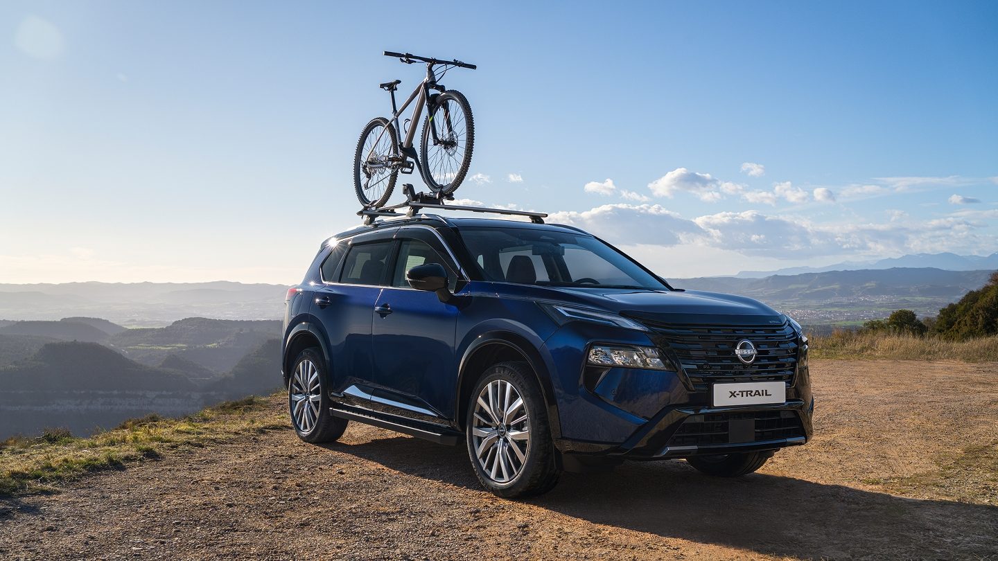 Blauer Nissan X-Trail mit Fahrradträger und Mountainbike auf einem Aussichtspunkt mit Blick auf die Berglandschaft