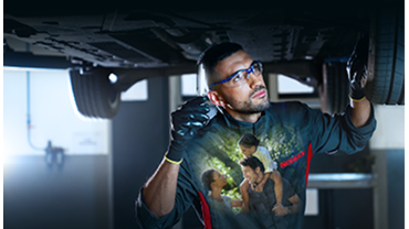 Ein Nissan Techniker arbeitet an einem Fahrzeug. Auf seinem T-Shirt ist eine glückliche dreiköpfige Familie abgebildet.