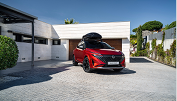 Ein Nissan Qashqai mit Dachbox als Zubehör steht vor einer Garage.