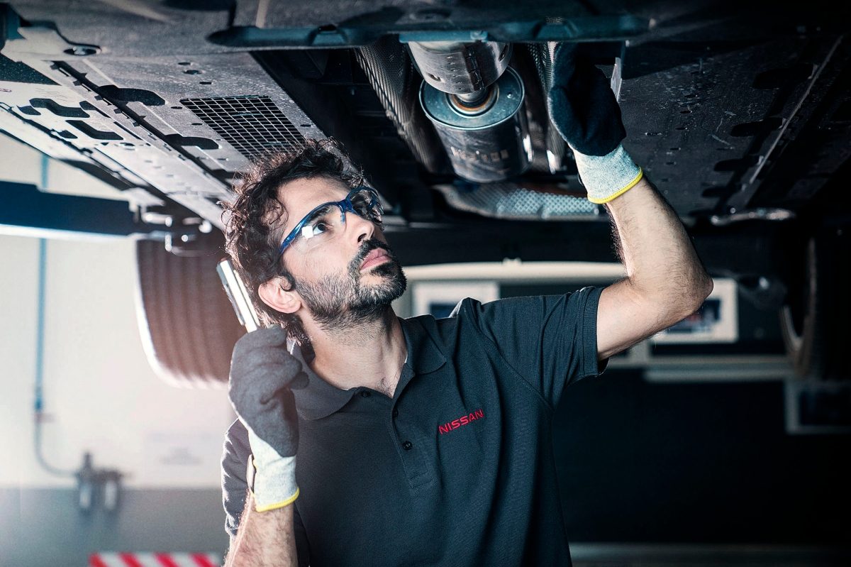 Ein Nissan Techniker kontrolliert Bauteile am Fahrzeug in der Werkstatt.