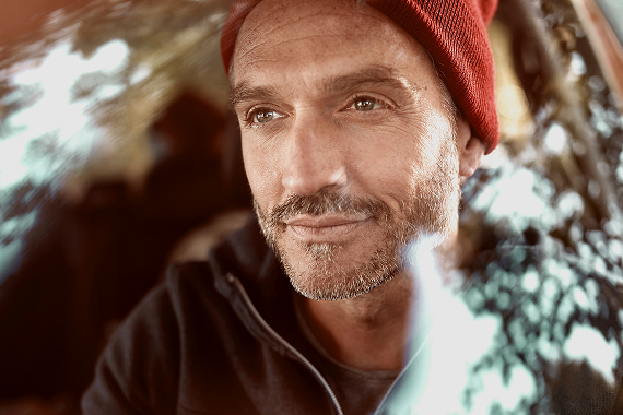 Ein Mann mit rotem Beanie sitzt zufrieden lächelnd auf dem Fahrersitz – ein starkes Symbol für das Vertrauen in Nissan Original Teile und Services.