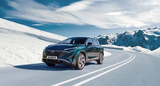 Nissan Qashqai in Deep Ocean mit schwarzem Dach fährt auf einer verschneiten Passstraße vor schneebedeckten Bergen