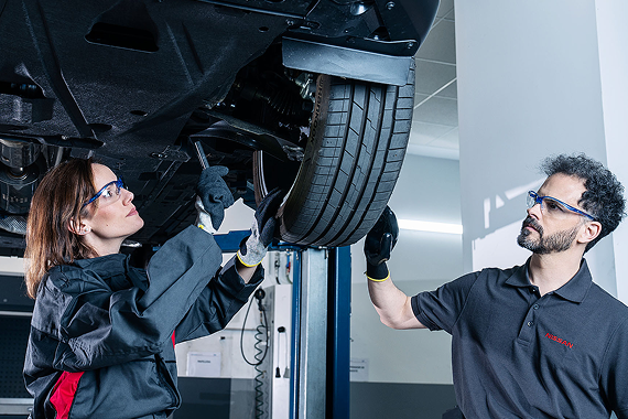 Zwei Mechaniker prüfen ein angehobenes Auto am Rad.