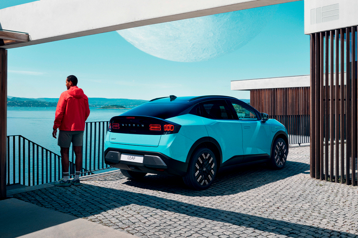 Ein Mann steht neben einem blauen Nissan LEAF, der an einer Ladestation geladen wird.