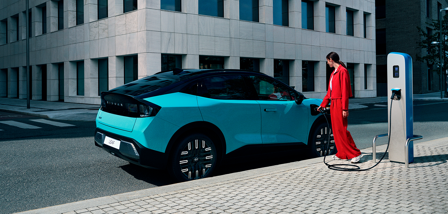 Frau lädt neuen Nissan LEAF an öffentlicher Ladestation in urbaner Umgebung