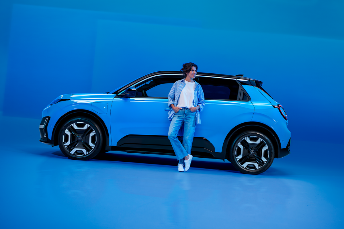 Der neue Nissan MICRA in einem Studio vor blauem Hintergrund, eine Frau lehnt lässig am Fahrzeug.