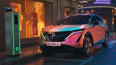 Nissan Ariya SUV eléctrico en color gris, diseño futurista con líneas aerodinámicas, estacionado en un entorno urbano moderno