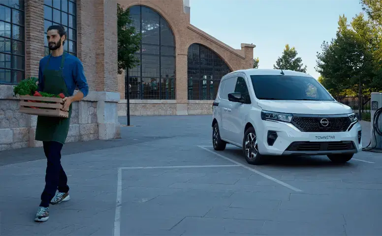 Un hombre sosteniendo una maceta al lado de un vehículo de la gama comercial de Nissan