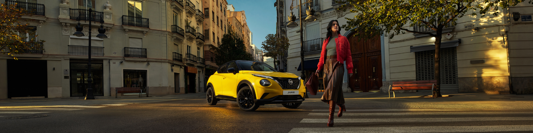 Nissan Juke híbrido amarillo circulando por ciudad con mujer pasando por paso de peatones