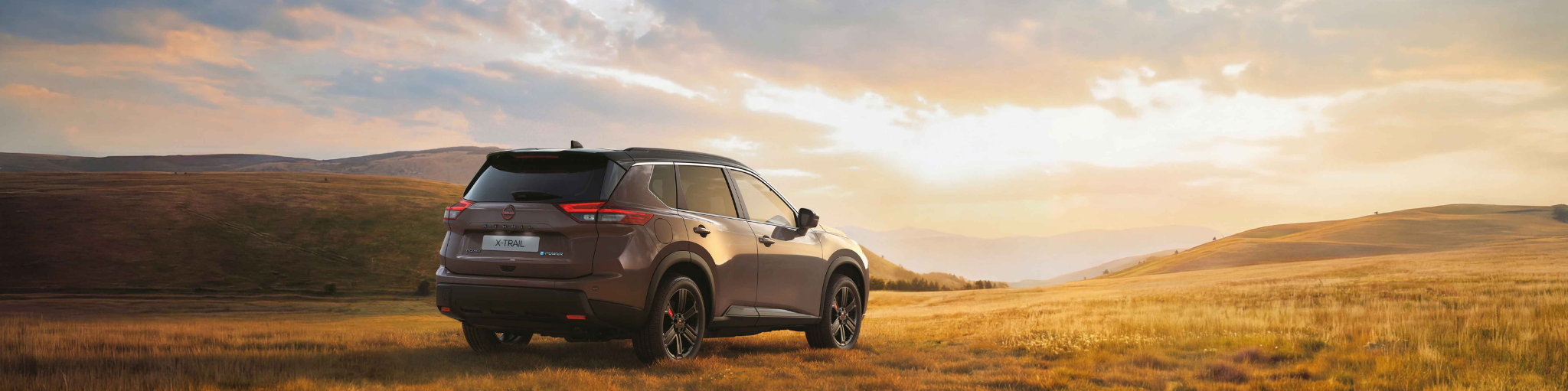 Nissan X-Trail de espaldas en un campo con amanecer en el cielo