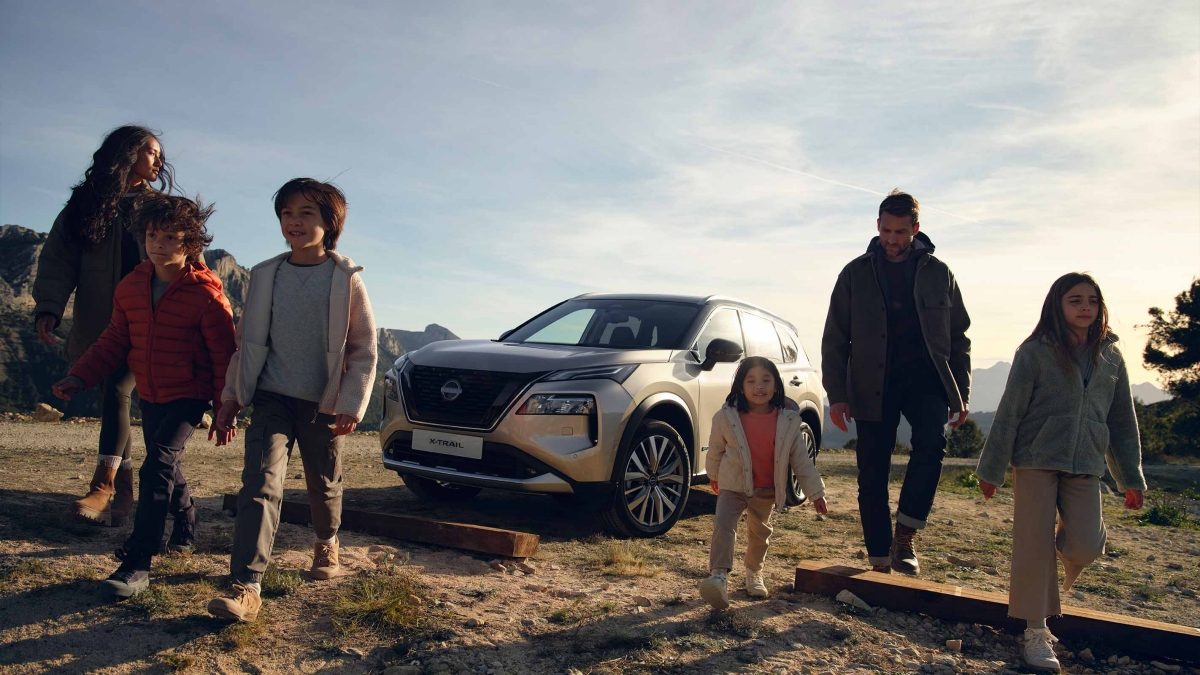 Una familia delante de un Nissan estacionado en la montaña