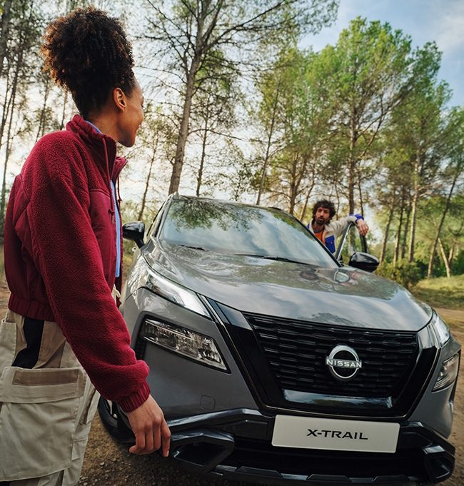 Nissan X-Trail en bosque con mujer fuera del coche