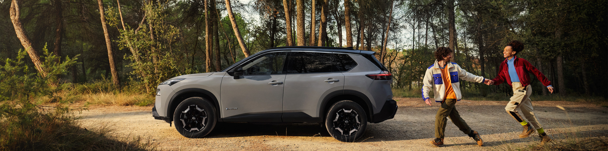 Nissan X-Trail en bosque con dos personas corriendo al lado. 