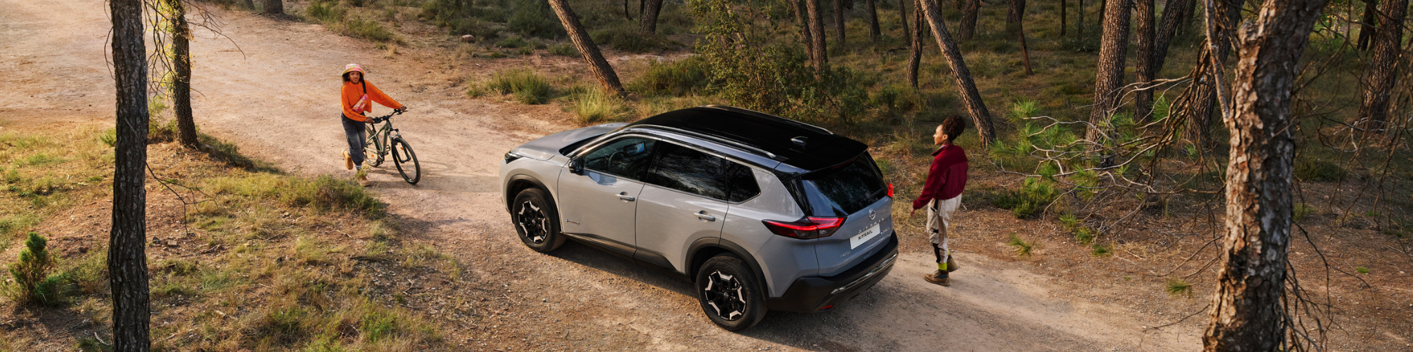 Nissan X-Trail con paisaje de montañas de fondo y mujer al lado del coche. 