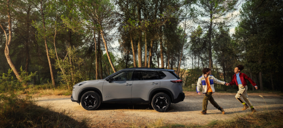 Nissan X-trail en bosque con dos personas corriendo alrededor