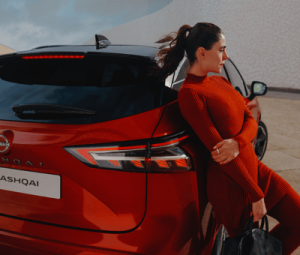 Mujer vestida de rojo junto a un Nissan Qashqai e-POWER
