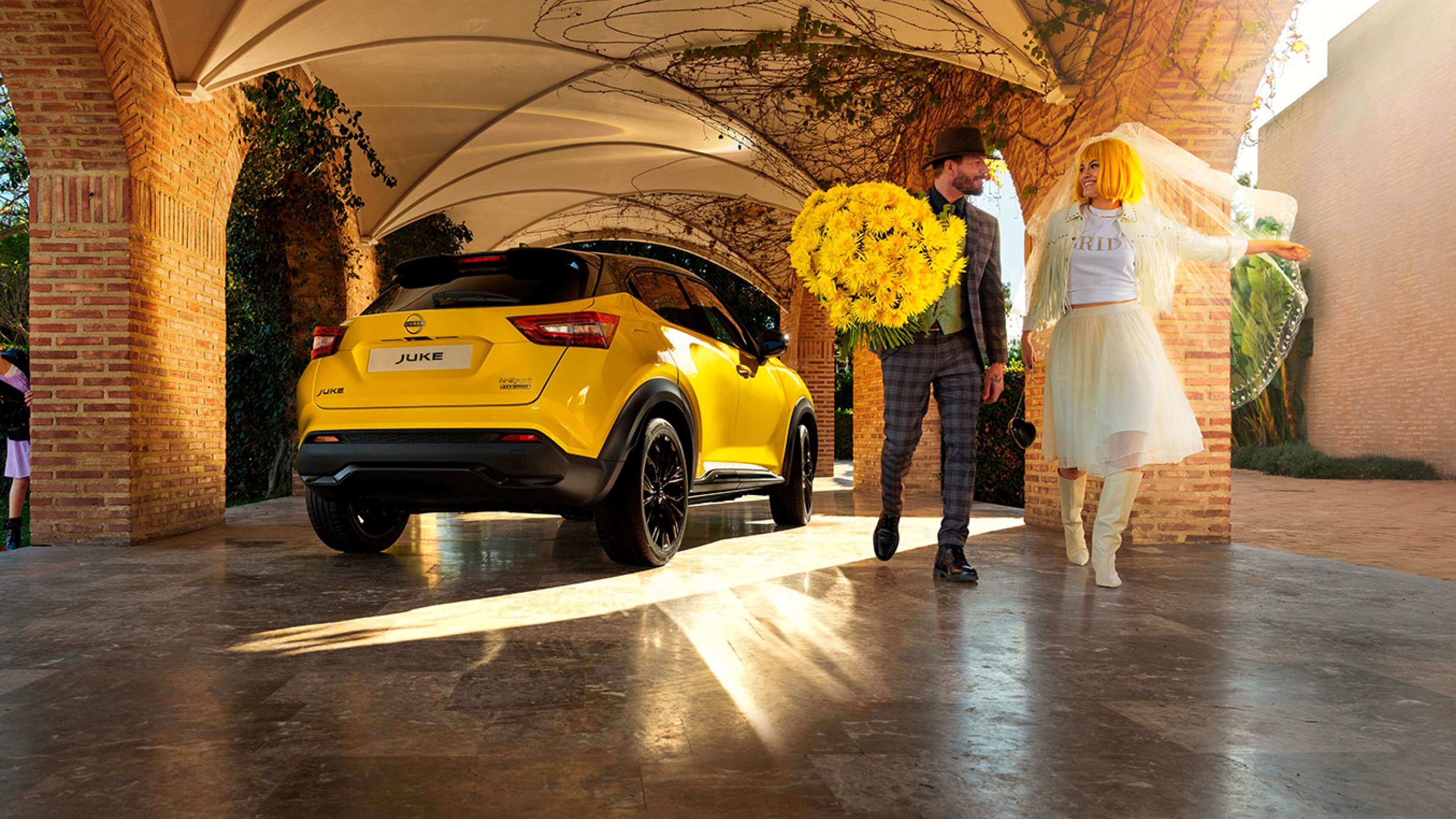 Vista trasera 3/4 del Nissan JUKE aparcado y una pareja de recién casados alejándose