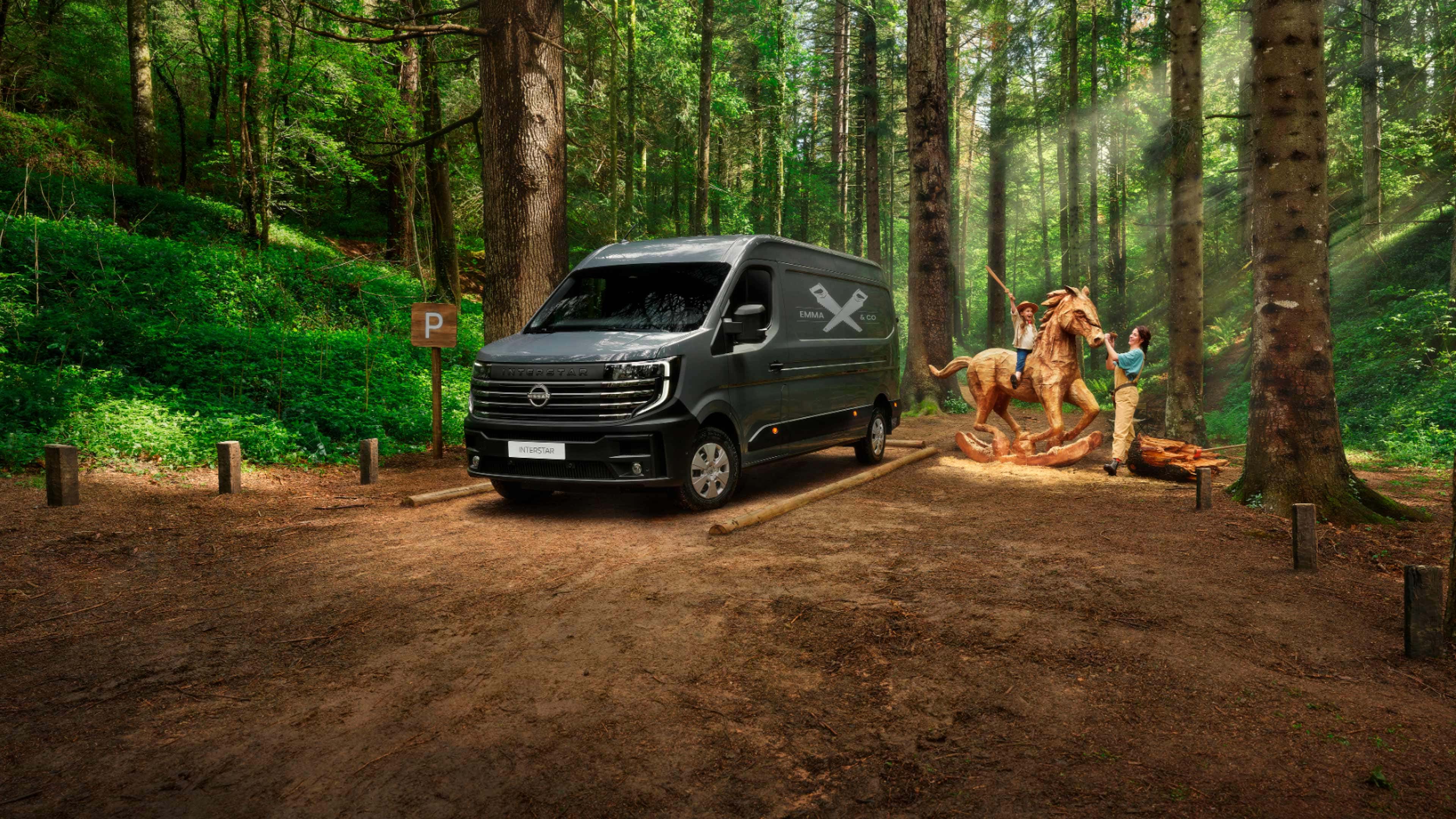 Vista frontal 3/4 de la furgoneta Nissan INTERSTAR aparcada y una familia jugando alrededor de un caballo de madera 