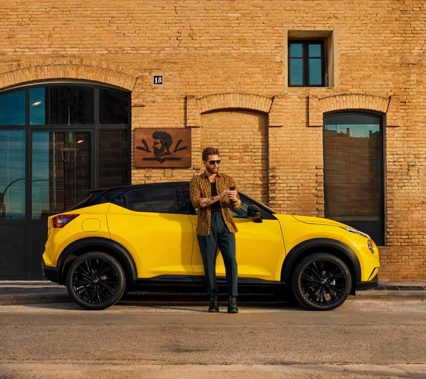 Vista de perfil de un Nissan Juke aparcado junto a una tienda con una persona de pie en el exterior sosteniendo un teléfono