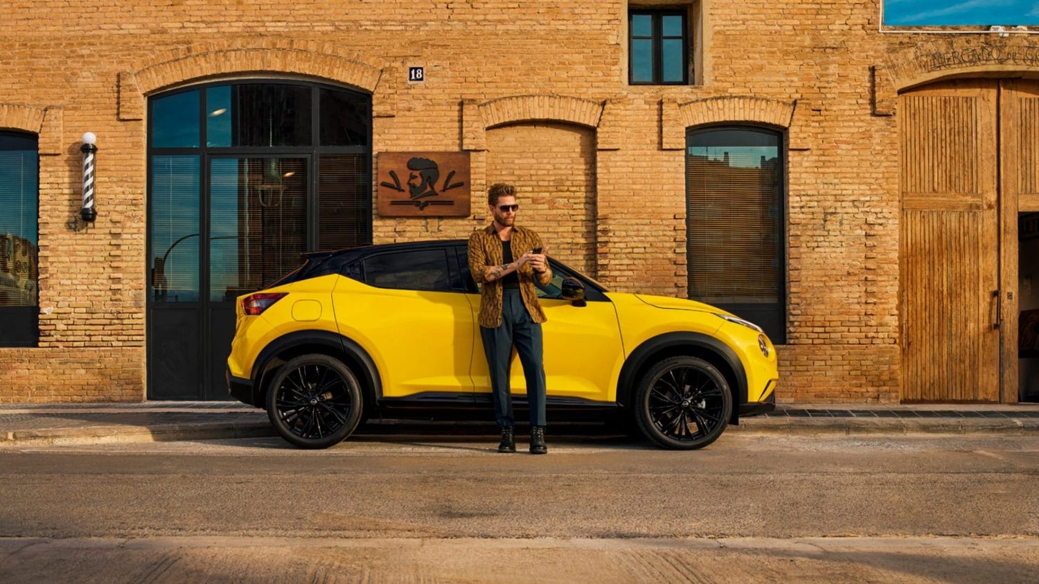 Vista frontal completa de un Nissan JUKE aparcado junto a una tienda con una persona de pie en el exterior sosteniendo un teléfono