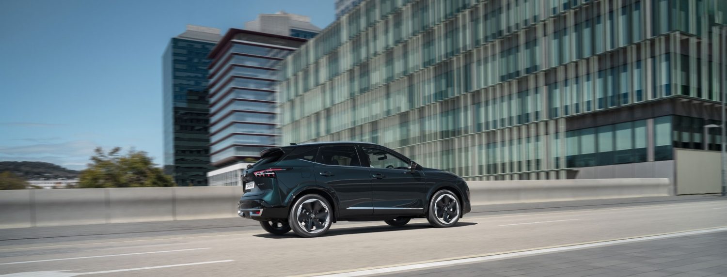 Nissan Qashqai de profil roulant devant une maison en plein soleil
