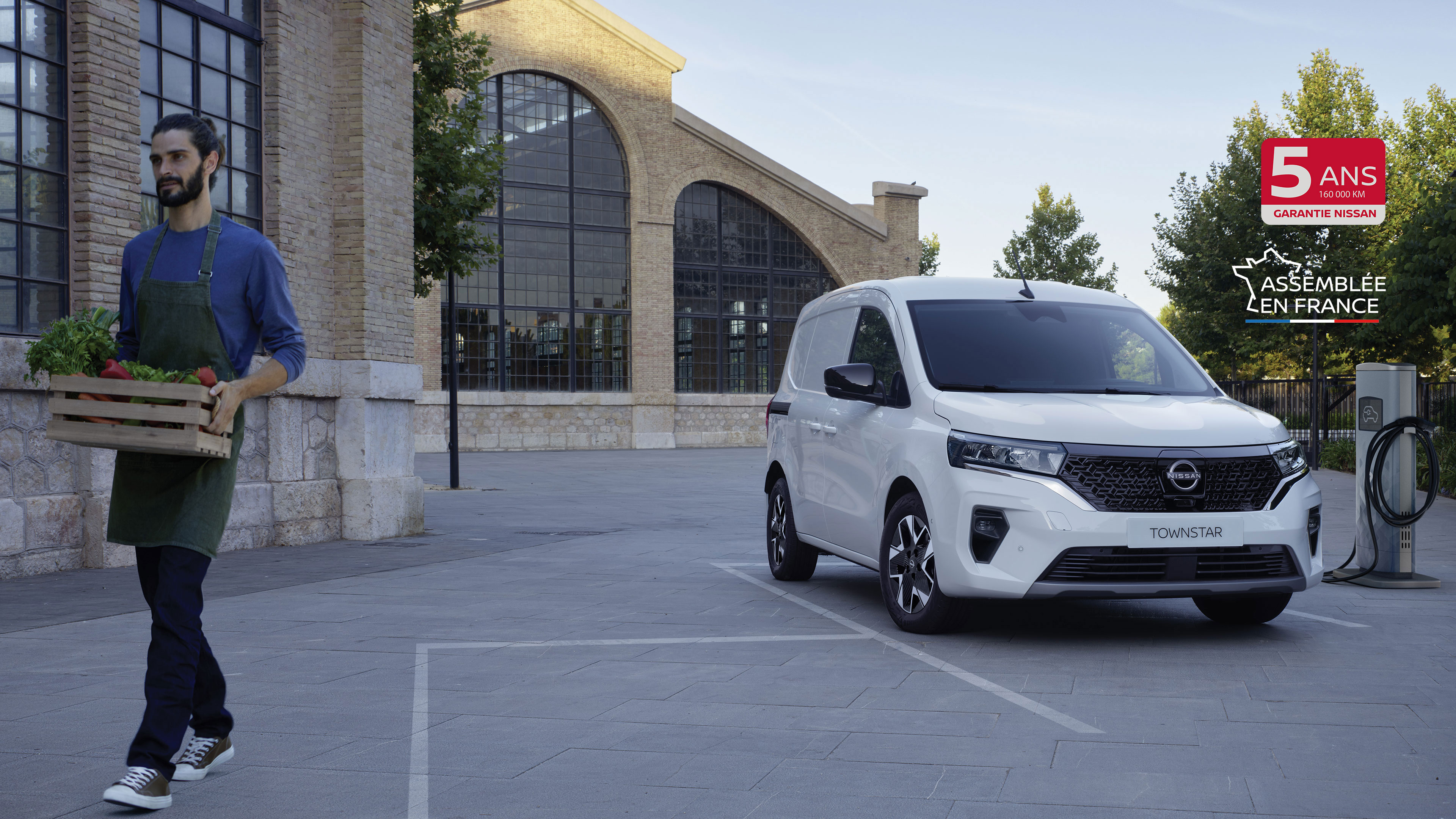 Nissan Townstar Fourgon de 3/4 face sur un parking près d'une borne de recharge