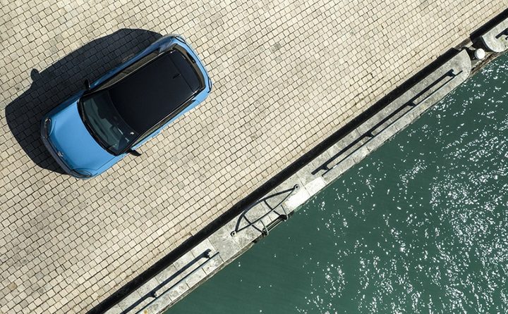 Blå Nissan MICRA elbil holder ved et fodgængerfelt nær en togstation eller offentlig transportknudepunkt.