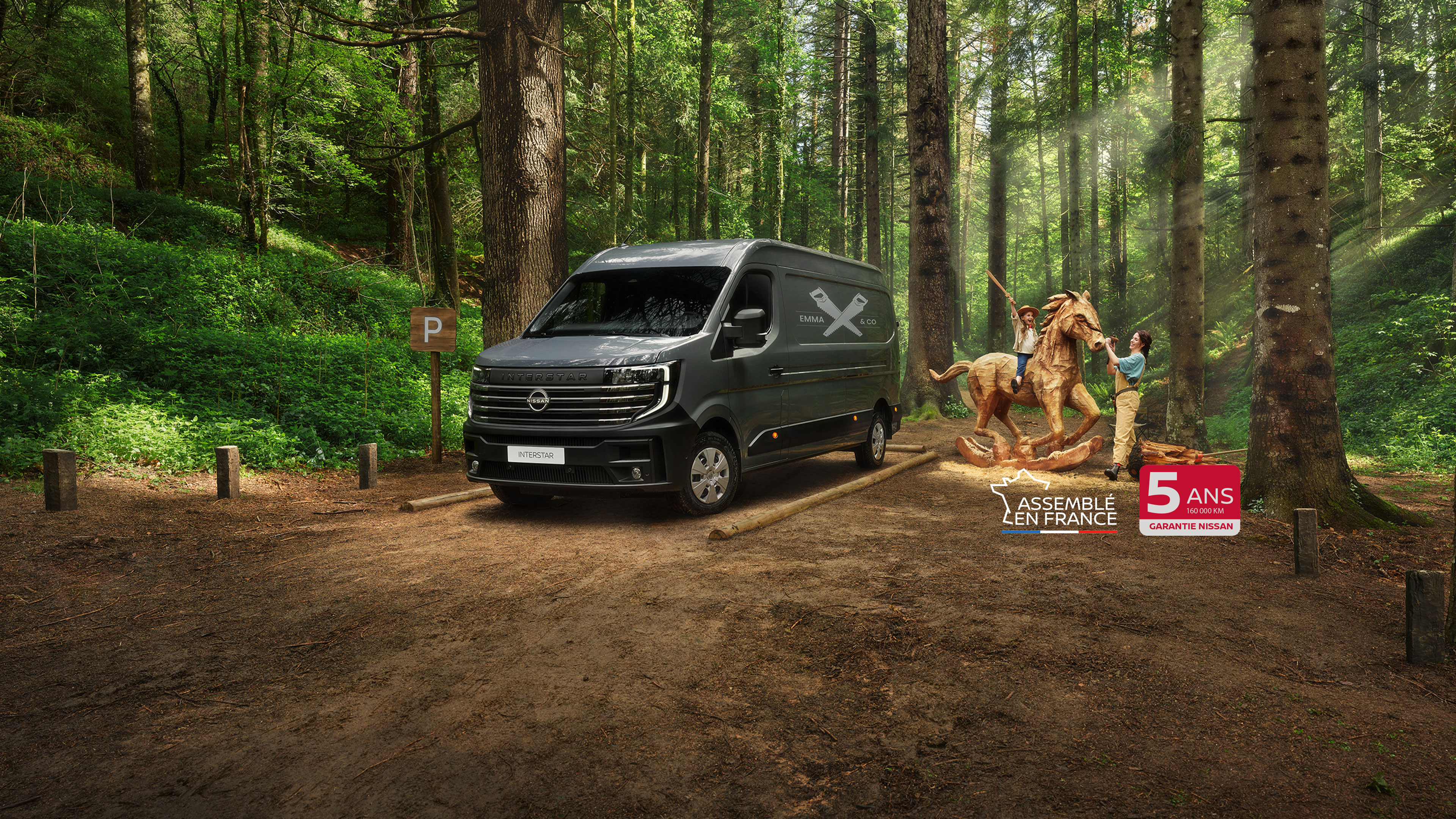 Nissan INTERSTAR fourgon 3/4 face stationné dans une forêt et famille jouant autour d’un cheval de bois  