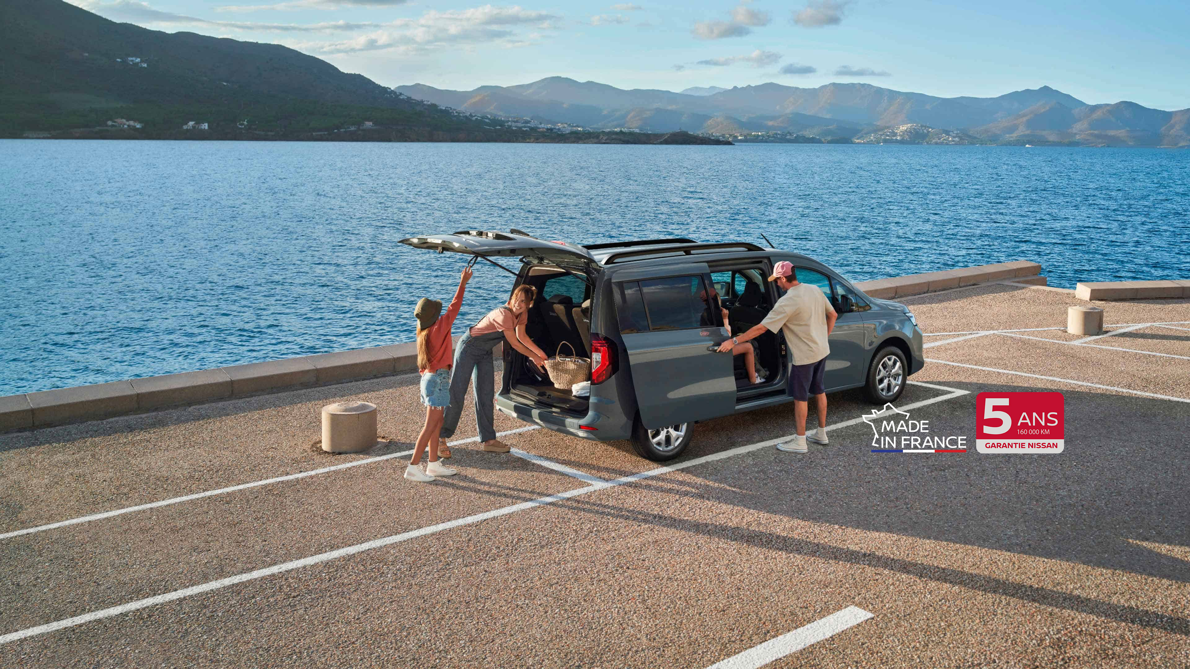 Nissan TOWNSTAR Combi : vue 3/4 arrière roulant sur route de montagne avec vue sur la mer
