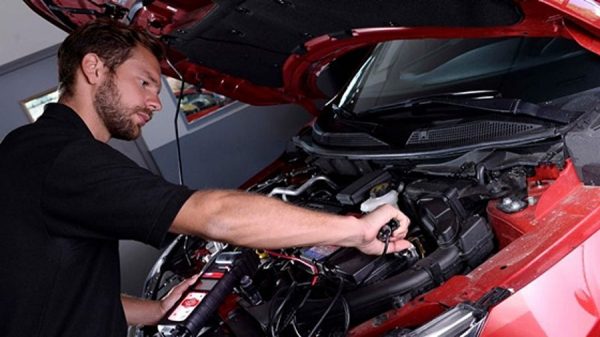 A blue nissan Qashqai lifted in a service centre with two technicians working on the undercarriage