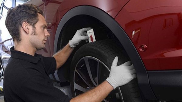 A blue nissan Qashqai lifted in a service centre with two technicians working on the undercarriage