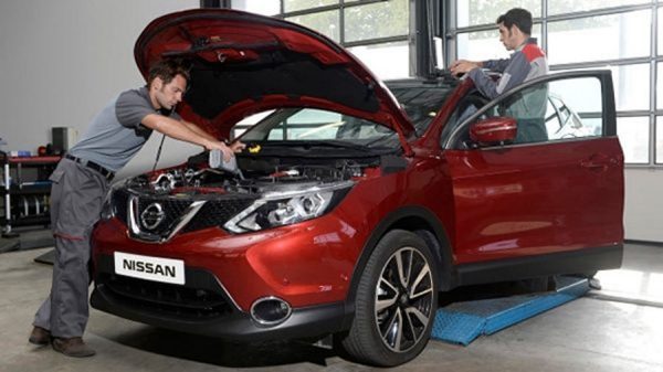 A blue nissan Qashqai lifted in a service centre with two technicians working on the undercarriage