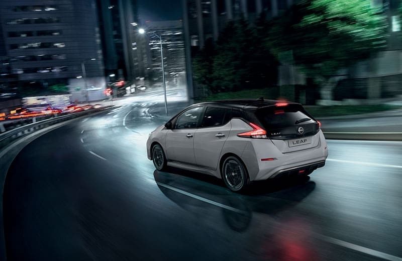מבט מאחור על ניסאן Leaf e+ בנסיעה בעיר בלילה