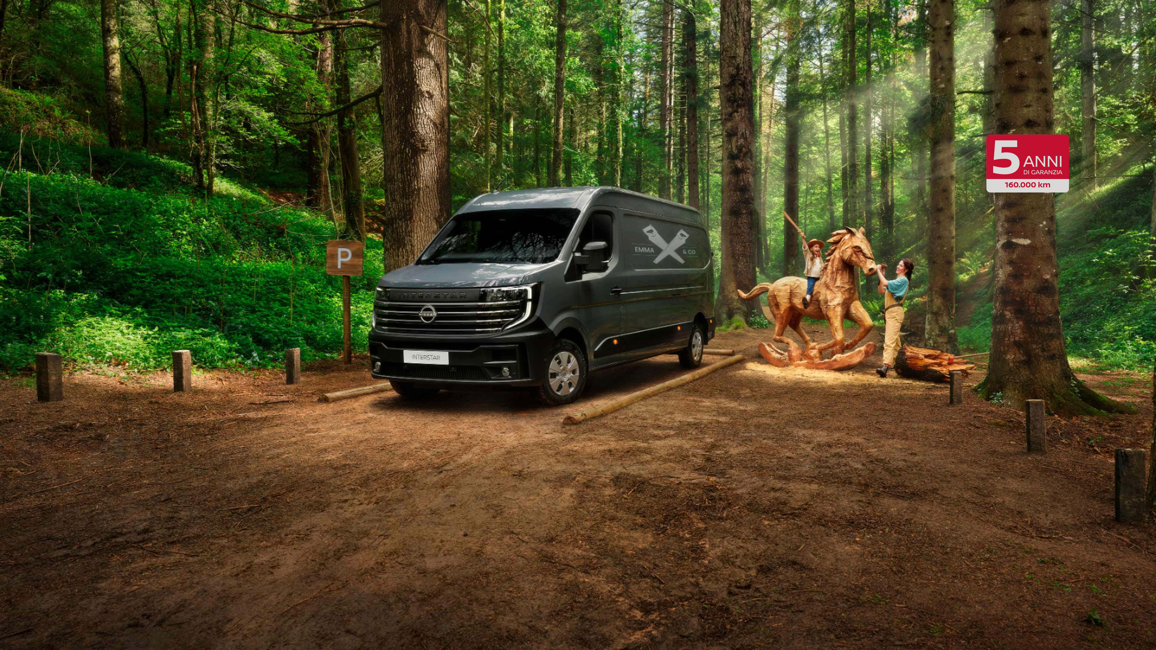  Immagine frontale a 3/4 di Nissan INTERSTAR parcheggiato in una foresta con una famiglia che gioca attorno a un cavallo di legno 