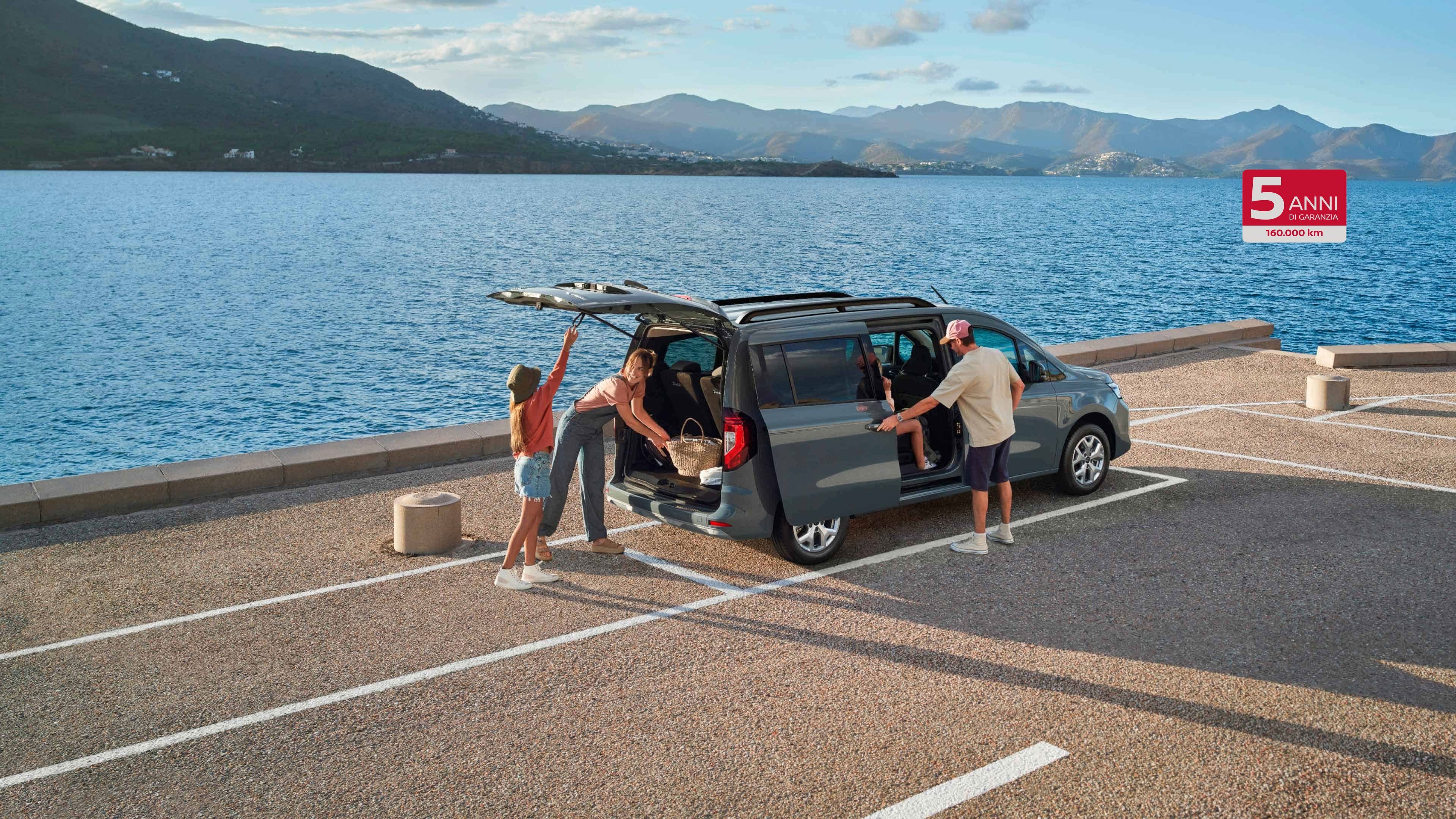 Nissan TOWNSTAR Combi: immagine frontale a 3/4 di un combi parcheggiato sulla spiaggia con una coppia con tavole da surf che guarda il mare al tramonto